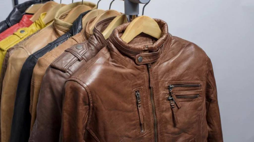 Leather jacket hanging to air dry on wide padded hanger in shaded room.