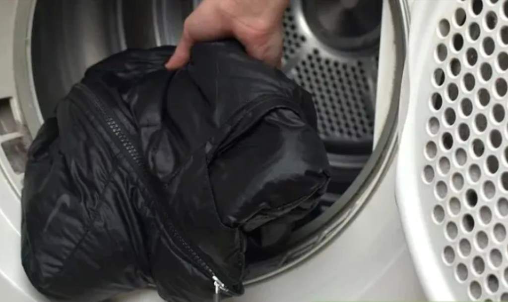 Person loading black leather jacket into front-load washing machine on delicate cycle.